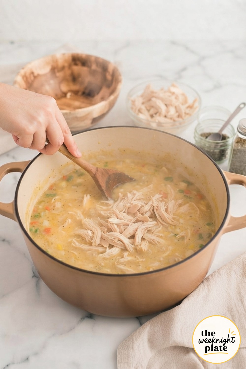 Stirring shredded chicken into thickened, simmering chicken pot pie soup as it turns creamy and golden